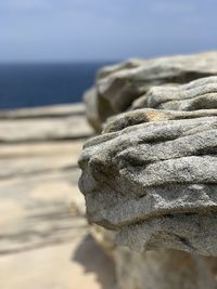 Close-up of pebbles on rock at beach against sky