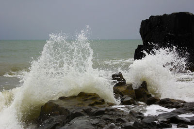 Waves splashing on rocks against clear sky