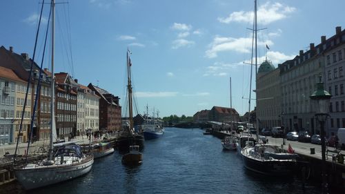 Sailboats in canal amidst buildings in city against sky