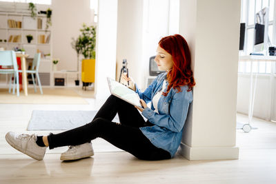 Side view of young woman sitting on hardwood floor at home