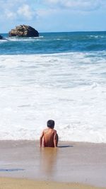 Full length of shirtless boy on beach against sky