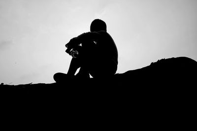 Low angle view of silhouette man sitting against sky