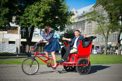 Happy couple traveling in pedicab on street during sunny day