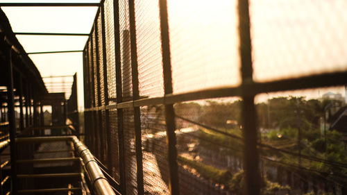 Metal railing by buildings against sky during sunset