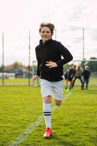 Cheerful teenage football player in activewear and boots running along field during training in summer