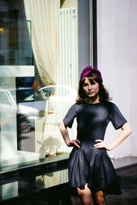 Beautiful young woman in black dress standing by building