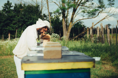 Side view of beekeeper examining beehive on land