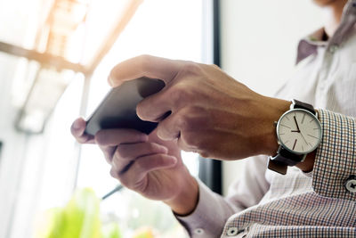 Midsection of man using mobile phone while sitting indoors