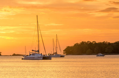 Sailboats sailing on sea against orange sky