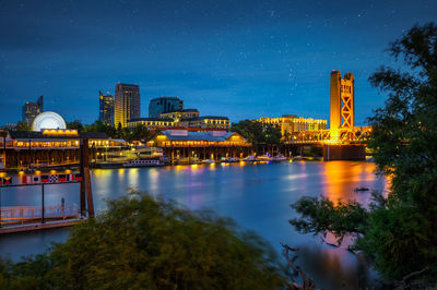 Buildings by river against sky at night