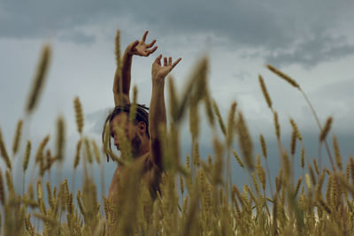 Shirtless young man with arms raised standing at farm