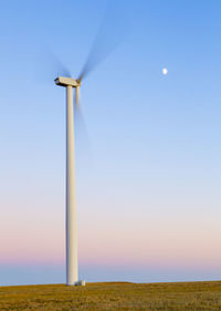 Wind turbine in motion against blue sky with moon