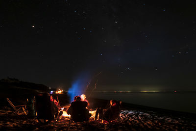 People sitting by fire against sky at night