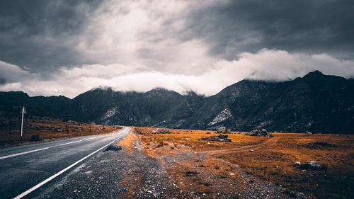 Empty road leading towards mountains against sky