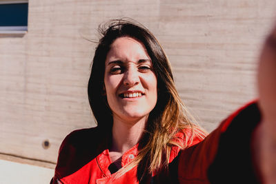 Portrait of smiling young woman standing against wall