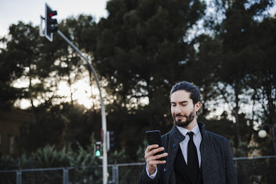Young man using mobile phone against trees