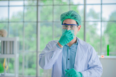 Portrait of scientist wearing surgical mask and cap standing in laboratory