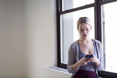 Businesswoman using mobile phone by window in new office