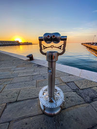 Coin-operated binoculars by sea against sky during sunset