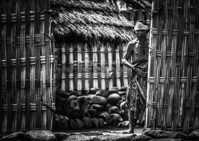 Portrait of shirtless man standing against hut