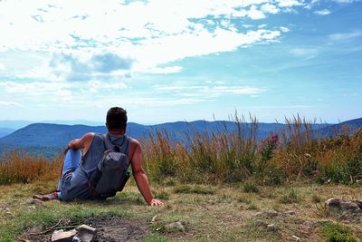 Rear view of man sitting on land against sky