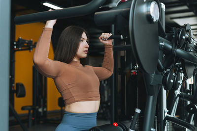 Young fitness brunette woman training for back muscles equipment at the gym