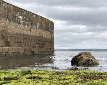 Stone wall by sea against sky