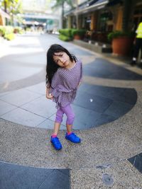 Portrait of cute girl standing with legs crossed at knee on street