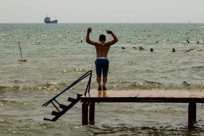 Rear view of shirtless man jumping into sea against sky