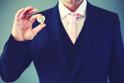 Midsection of businessman holding heart shape text against colored background