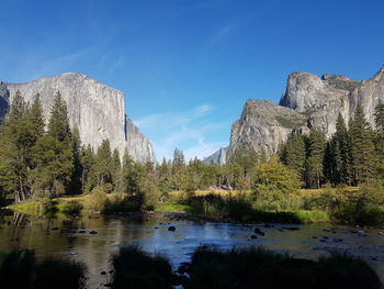 Scenic view of river by mountains against clear blue sky