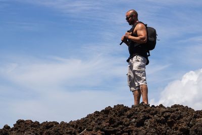 Low angle view of man standing on rock against sky