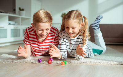 Cheerful siblings playing with dice while lying on carpet at home