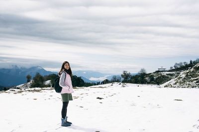 Young woman standing on snow covered field against cloudy sky