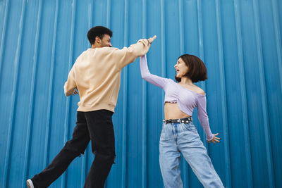 Side view of a young couple standing on blue wall