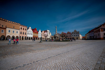 People on street by buildings in town against blue sky