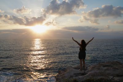 Rear view of woman standing at beach during sunset