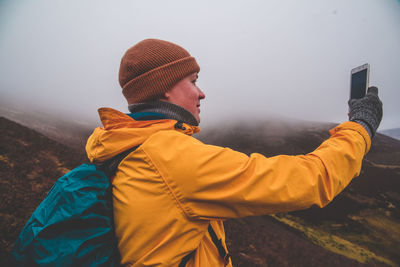 Side view of man wearing hat standing against sky during winter