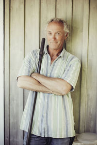 Portrait of confident man with shovel standing arms crossed against wall