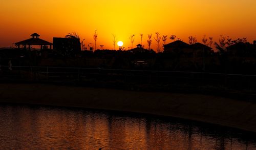 Silhouette bridge over lake against orange sky