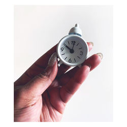 Close-up of hand holding clock against white background