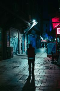 Rear view of man walking on footpath amidst buildings at night