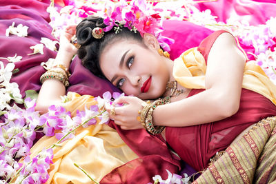 High angle view of beautiful woman wearing traditional clothing and jewelry while lying with flowers on bed