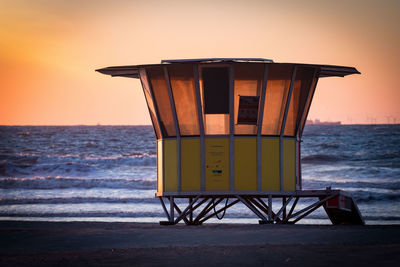 Lifeguard hut on beach against sky during sunset