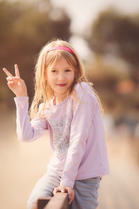 Portrait of girl gesturing peace sign while sitting on railing