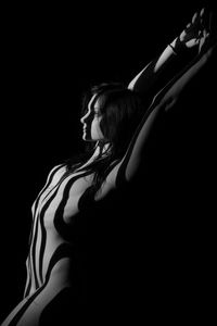 Side view of naked woman with arms raised standing against black background