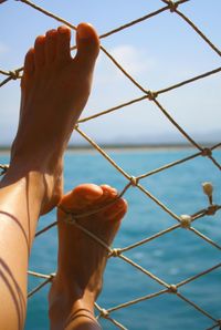 Low angle view of woman feet on net against sky