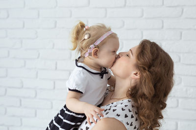 Side view of mother kissing daughter against wall