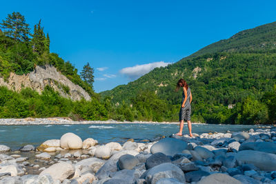 Full length of man standing on rock against blue sky