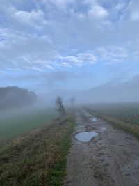 Scenic view of rural road against foggy sky